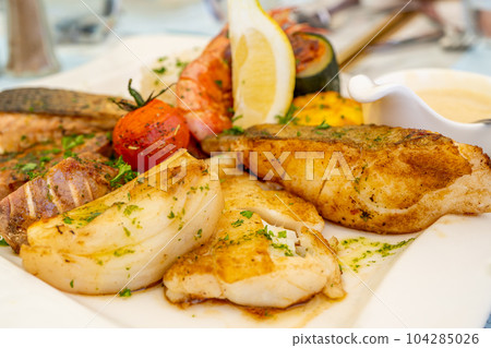 Grilled delicious fish fillets and shrimps with vegetables and lemon slices. Mediterranean diet. 104285026
