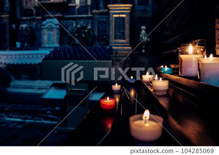 Candles in the Catholic Church. Beautiful glass windows with the evening light on the background. Candles in the Catholic Church. Beautiful glass windows with the evening light on the background. 104285069