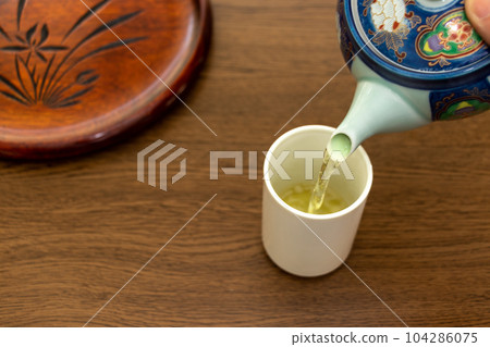 Pour hot tea from a teapot into a cup 104286075