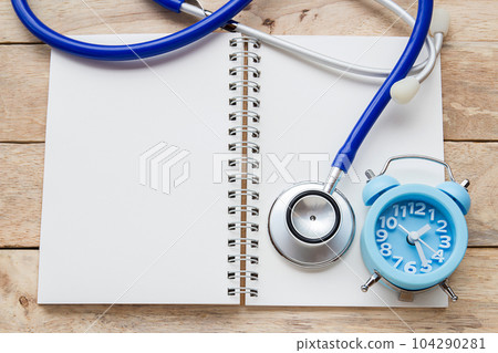 Top view of blank notebook,alarm clock and blue stethoscope equipment on wood table background. 104290281