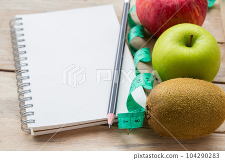 Healthy lifestyle concept with red apple. Weight loss or diet concept. Red apple and green measure tape,kiwi,carrot on wood table background Healthy lifestyle concept with red apple. Weight loss or diet concept. Red apple and green measure tape,kiwi,carrot on wood table background 104290283