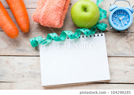 Top view carrot with blue stethoscope,measuring tape,apple,alarm clock and notebook on wood table background. Top view carrot with blue stethoscope,measuring tape,apple,alarm clock and notebook on wood table background. 104290285
