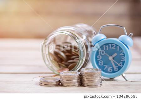 Close up saving money into a glass jar and alarm clock for cash in future investment. Close up saving money into a glass jar and alarm clock for cash in future investment. 104290583