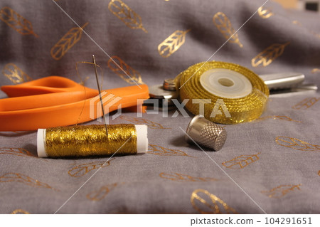 Spool of Metallic Gold Thread on Gray and Gold Chiffon Fabric Spool of Metallic Gold Thread on Gray and Gold Chiffon Fabric 104291651