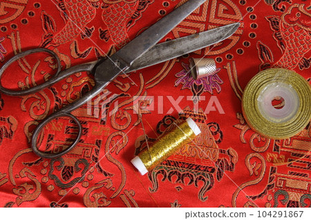 Spool of Gold Metallic Thread and Thimble on Vintage Red Silk Fabric Spool of Gold Metallic Thread and Thimble on Vintage Red Silk Fabric 104291867