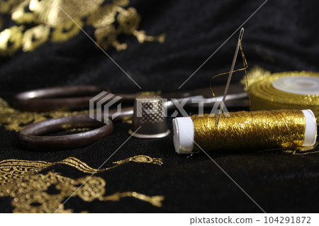 Spool of Gold Thread With Thimble on Metallic Fabric 104291872