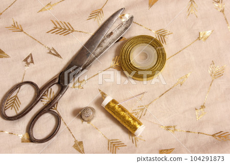 Spool of Gold Thread and Scissors With Thimble on Metallic Fabric Spool of Gold Thread and Scissors With Thimble on Metallic Fabric 104291873