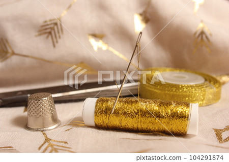 Spool of Gold Thread and Scissors With Thimble on Metallic Fabric Spool of Gold Thread and Scissors With Thimble on Metallic Fabric 104291874