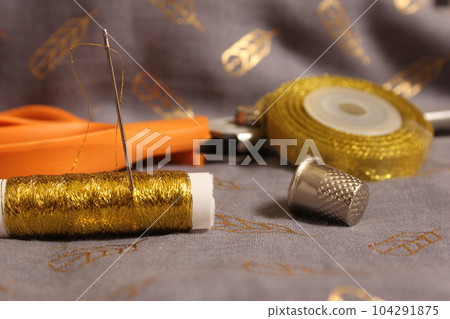 Spool of Metallic Gold Thread on Gray and Gold Chiffon Fabric 104291875