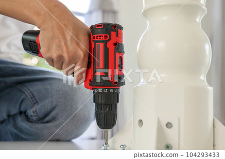 man assembling white table furniture at home using cordless screwdriver man assembling white table furniture at home using cordless screwdriver 104293433
