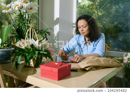 Portrait of female florist entrepreneur freelancer writing notes on clipboard, drawing composition of flowers for special events, sitting at table in her home flower shop. Business. Creativity. People Portrait of female florist entrepreneur freelancer writing notes on clipboard, drawing composition of flowers for special events, sitting at table in her home flower shop. Business. Creativity. People 104295482