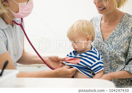 Infant baby boy child being examined by his pediatrician doctor during a standard medical checkup in presence and comfort of his mother. National public health and childs care care koncept 104297430
