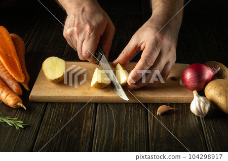 The cook cuts the potatoes in the kitchen with a knife to prepare a national dish or mashed potatoes. Delicious vegetable diet. The cook cuts the potatoes in the kitchen with a knife to prepare a national dish or mashed potatoes. Delicious vegetable diet. 104298917
