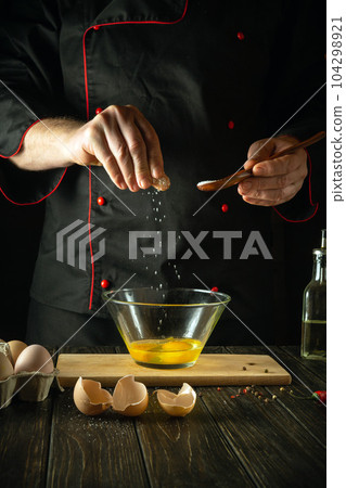 The chef adds salt while cooking the eggs. Work environment on the kitchen table. Menu idea for a restaurant or hotel. The chef adds salt while cooking the eggs. Work environment on the kitchen table. Menu idea for a restaurant or hotel. 104298921