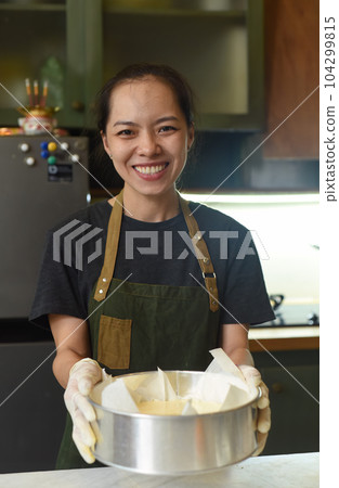 Vietnamese woman holding a baking dish with cheesecake dough in the kitchen Vietnamese woman holding a baking dish with cheesecake dough in the kitchen 104299815