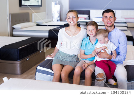 Happy family sitting on bed in store Happy family sitting on bed in store 104300184