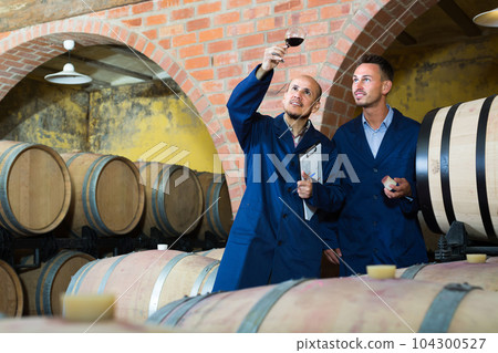 two winemakers with sample of wine in cellar. 104300527