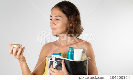 A woman after a shower with a cosmetic bag in her hands - chooses a cream, self-care at home 104300564