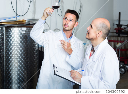 two men coworkers in white coats working in fermentation section 104300592
