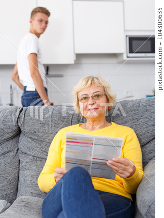Woman reading booklet on sofa 104300635