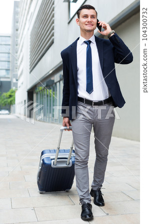 Successful businessman in suit with suitcase is talking by phone Successful businessman in suit with suitcase is talking by phone 104300732