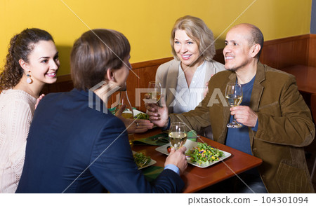 Four adults with wine and dinner laughing in restaurant 104301094