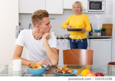 Guy sitting while his mother cooking breakfast 104301096