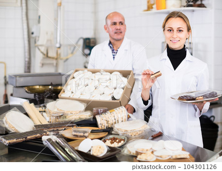 Different aged couple standing with box of turron in production workshop 104301126
