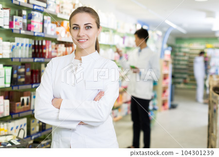 Woman pharmacist is standing welcoming in pharmacy Woman pharmacist is standing welcoming in pharmacy 104301239