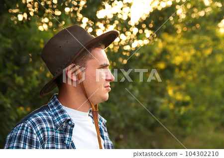 A young farmer in a cowboy hat stands proudly in an agricultural field, surrounded by the beauty of nature. With a closeup portrait capturing his determined expression, hardworking rancher. Copy space 104302210