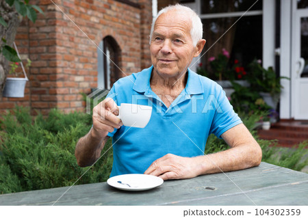 Old man sitting at table in outdoor cafe and drinking tea Old man sitting at table in outdoor cafe and drinking tea 104302359