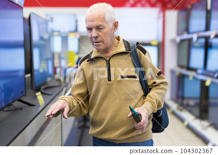 elderly grayhaired man pensioner looking counter with modern digital televisors in showroom of digital goods store elderly grayhaired man pensioner looking counter with modern digital televisors in showroom of digital goods store 104302367