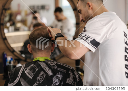 Back view of human hand hold trimmer and make hairstyle for man. Barbershop  104303595