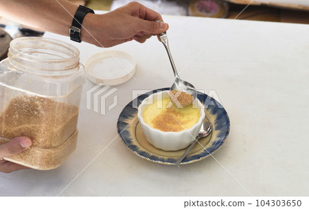 Process of sprinkling brown sugar on the Creme brulee on white background Process of sprinkling brown sugar on the Creme brulee on white background 104303650