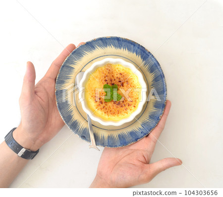 Hands holding a dish with Creme brulee on white background Hands holding a dish with Creme brulee on white background 104303656