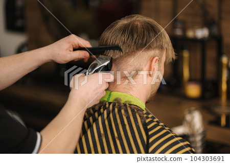 Back view of barber using trimmer to make haircut for customer Back view of barber using trimmer to make haircut for customer 104303691