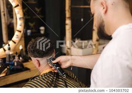 Man sitting in barber shop during barber have cut his hair. Back view of process  104303702