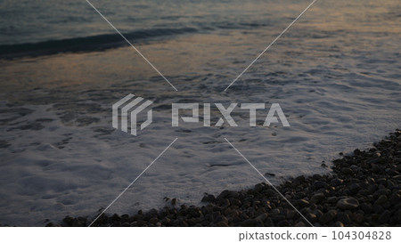 waves on a pebble beach at sunset 104304828