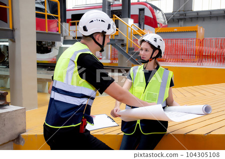 Young caucasian engineer man and woman or worker looking blueprint and checking electric train. 104305108