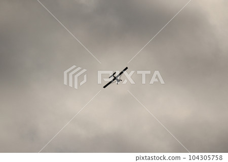 Small plane flying in the sky against dark clouds 104305758