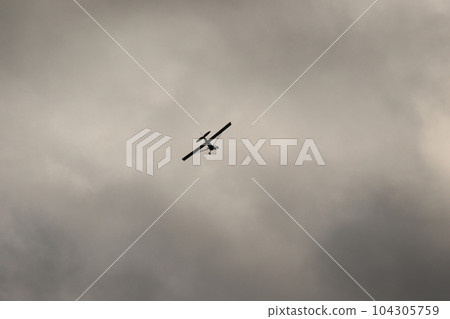 Small plane flying in the sky against dark clouds 104305759