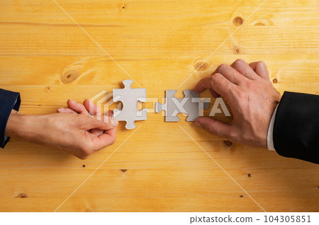 Hands of business partners matching two blank puzzle pieces Hands of business partners matching two blank puzzle pieces 104305851