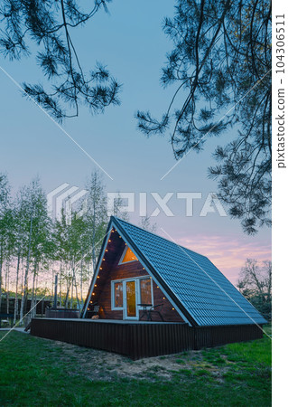 A-frame wooden cabin with light inside in evening 104306511