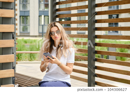 Woman in sunglasses on bench with smartphone 104306627