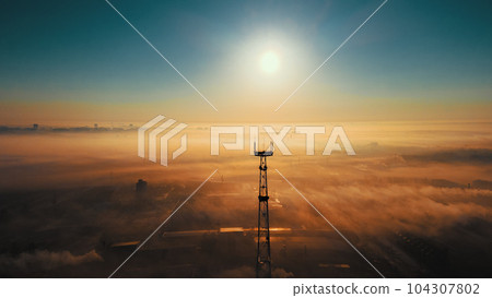 Landscape from drone. Sun on horizon line and fog over industrial industrial zone. Communication 104307802
