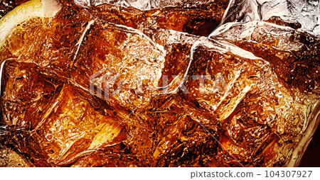 Cola with Ice. Close up of the ice cubes in cola water. Texture of carbonate drink with bubbles in glass. Cola soda and ice splashing fizzing or floating up to top of surface. Cold drink background. Cola with Ice. Close up of the ice cubes in cola water. Texture of carbonate drink with bubbles in glass. Cola soda and ice splashing fizzing or floating up to top of surface. Cold drink background. 104307927