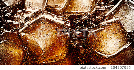 Cola with Ice. Close up of the ice cubes in cola water. Texture of carbonate drink with bubbles in glass. Cola soda and ice splashing fizzing or floating up to top of surface. Cold drink background. Cola with Ice. Close up of the ice cubes in cola water. Texture of carbonate drink with bubbles in glass. Cola soda and ice splashing fizzing or floating up to top of surface. Cold drink background. 104307935