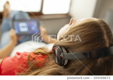 Woman sitting in armchair near a window and listening to music using headphones 104308672