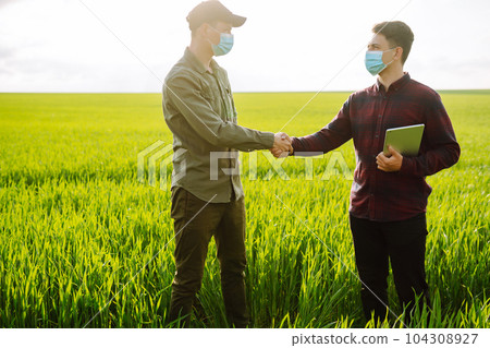 Two Farmers in protection mask with tablet in the field. Modern agriculture technology.Smart farming Two Farmers in protection mask with tablet in the field. Modern agriculture technology.Smart farming 104308927