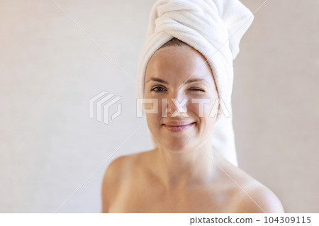 Woman with a towel wrapped around her head winking and looking at camera Woman with a towel wrapped around her head winking and looking at camera 104309115